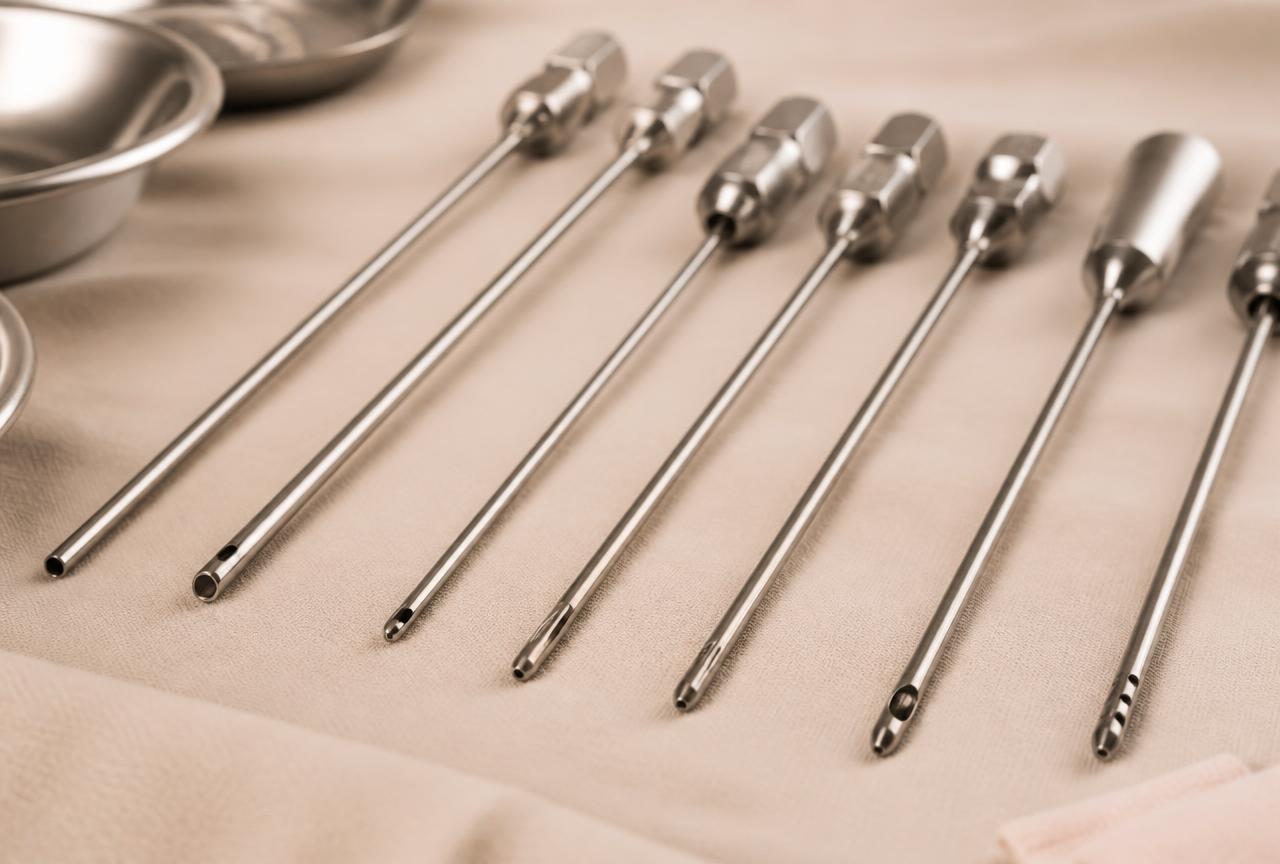 Canules de liposuccion en acier de différents diamètres et embouts, alignées sur un champ stérile